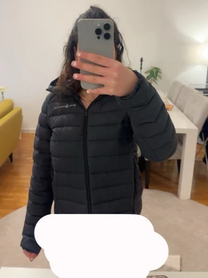 Svart dunjacka från sail racing  - Säljer en svart dunjacka från Sail racing i storlek M med huva och dragkedja framtill. Jackan har diskret logga på bröstet och en rund logga på ryggen. Perfekt för kalla dagar och riktigt skön att bära. Klassisk quiltad design och stilren look. Säljer pga att jag köpte en ny jacka men denna är nästan helt ny och använd i bara ca 4 månader ! 