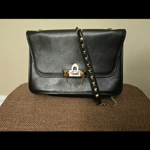 Svart Valentino Garavani Rockstud Demi-Lune Axelväska - Autentisk Valentino Garavani Rockstud Demi-Lune Axelväska – Svart & Guld  Limiterad upplaga av Valentino Rockstud Demi-Lune axelväska i svart läder med gulddetaljer. Ikonisk halvmåneformad silhuett med signaturpyramidnitar. Inkluderar original Valentino-presentask och äkthetskort. Digital kopia av originalkvitto från Valentino Saint-Tropez (09/09/2017, 1 400 €). Utmärkt skick. Tidlös lyxklassiker till ett bra pris.