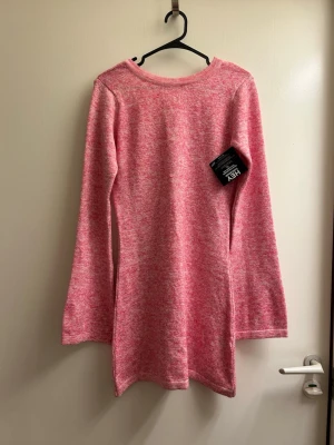 Rosa stickad tröja med vid ringning - Mysig rosa stickad tröja från Nelly med melerad effekt. Tröjan har lång ärm, vid rundad ringning och en något längre, rak passform. Perfekt för dig som gillar en avslappnad men ändå söt stil.