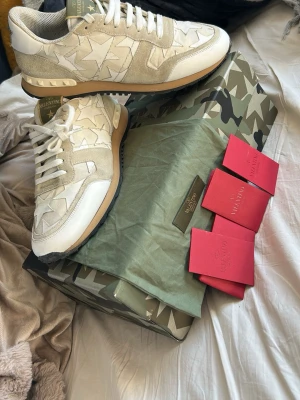 Valentino Garavani beige sneakers - Snygga sneakers från Valentino Garavani i beige och vitt med stjärnmönster på sidorna. Skorna har en mix av mocka och textil, vita snören och en beige sula med gummidetaljer. Kommer med originalkartong och dustbag i camomönster.anvönda ett fåtal gånger men mycket bra skick allt ingår förutom box
