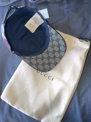 Gucci keps med GG-mönster - Säljer en snygg Gucci keps i beige och marinblått med det klassiska GG-monogrammet över hela kepsen. Kepsen har justerbar rem bak och detaljer i rött och blått på sidan. Materialet är canvas och insidan är fodrad i mörkt tyg. Dustbag från Gucci medföljer. GG paket med också 👍🏻