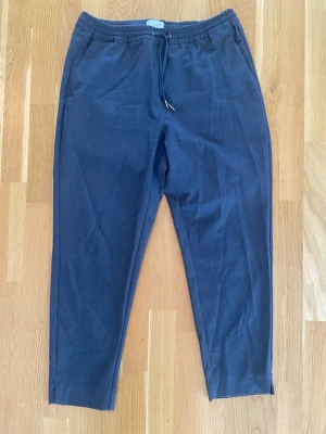 Mörkgrå byxor med dragsko strl M - Lindex Holly & White byxor dam M grå modell Ava cropped tappers. Byxorna har resår i midjan och en liten slits längst ner på benet  Använda och något lite noppriga på några ställen i övrigt i bra begagnat skick.  Mått Midjan: ca 43 cm Längd från grenen och ner: ca 69 cm  65% polyester, 33% viskos och 2% elastan   Kommer från ett djur och rökfritt hem.