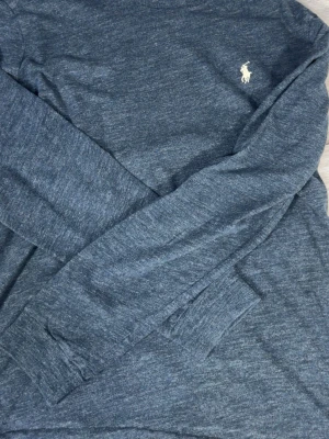 Mörkgrå långärmad tröja Polo Ralph Lauren - Mörkgrå långärmad tröja från Polo Ralph Lauren i custom slim fit. Tröjan har rund halsringning, diskret broderad logga på bröstet och är tillverkad i mjukt material. Perfekt för en clean och stilren look.