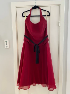 Röd långklänning med svart knytband - Säljer en elegant röd långklänning med halterneck och svart knytband i midjan. Klänningen har ett flytande, lätt transparent yttertyg och en vacker, svepande siluett. Perfekt för dig som vill sticka ut med en klassisk men modern look. Endast använd vid ett par tillfällen och förutom en liten tråd i nacken är klänningen i väldigt fint skick  Mått Över bröstet: ca 48 cm Längd från armhålan och ner: ca 98 cm Över midjan: ca 44 cm  100% polyester   Kommer från ett djur och rökfritt hem 