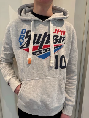 Grå hoodie från Superdry - Snygg grå hoodie från Superdry i storlek M. Modellen är 193 cm och väger 68 kg