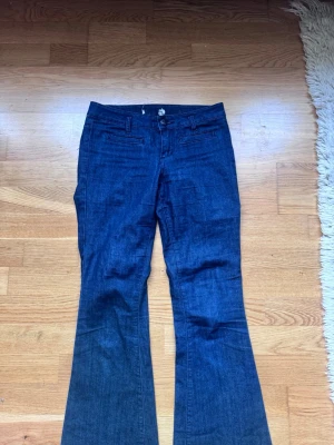 Mörkblå bootcut jeans - Snygga mörkblå bootcut jeans med klassisk femficksdesign och utsvängda ben. Jeansen har hällor för skärp och stängs med knapp och dragkedja. Perfekta för en trendig och avslappnad look. Innerbenslängd: 77 midjemått: 35 men är stretchiga