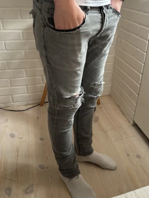 Dondup Jeans - Säljer ett par grå skinny jeans med slitningar och hål på knäna. Jeansen har en tvättad look, råa kanter vid fickor och bakfickor med detaljer. Perfekta för dig som gillar en edgy och avslappnad stil.