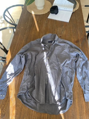 Grå skjorta från Massimo Dutti - Snygg grå skjorta från Massimo Dutti i mjukt bomullstyg. Klassisk krage, knappar framtill och lång ärm med knapp vid manschetten. Perfekt för en stilren och avslappnad look.