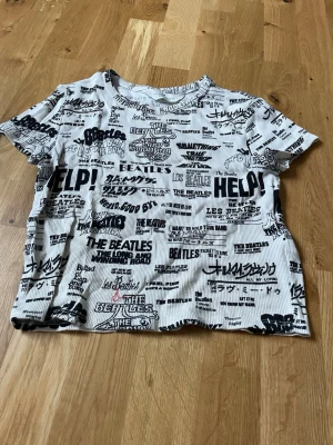 The Beatles t-shirt från H&M - Cool t-shirt från H&M med svartvitt The Beatles-tryck över hela plagget. T-shirten är ribbad, kortärmad och har en avslappnad passform. Perfekt för dig som gillar bandtröjor och vill sticka ut med ett unikt mönster.