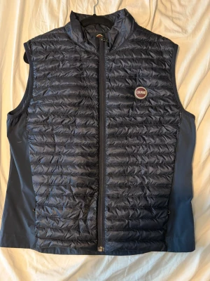 Mörkblå dunväst från Colmar - Snygg mörkblå dunväst från Colmar med quiltad framsida och diskret logga på bröstet. Västen har hög krage, dragkedja framtill och sidofickor med dragkedja. Perfekt lager på lager-plagg för kyliga dagar. Materialet är glansigt och lätt.