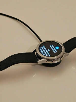 Samsung Galaxy Watch 4 Classic med extra armband - Samsung Galaxy Watch 4 Classic i silver med rund urtavla och svart silikonarmband. Flera extra armband i olika färger och material ingår, bland annat metall, tyg och silikon. Laddkabel och verktyg för byte av armband medföljer. Perfekt för dig som vill byta stil på din smartklocka. Allt är i använt med fullt fungerande och gott skick. 
