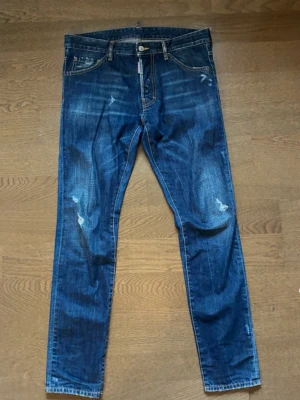 Blue denim DSQUARED2 jeans i modellen ”cool guy” - Säljer ett par denim blue jeans med snygga slitningar och tvättade detaljer. Jeansen har klassisk femficksmodell, knappgylf och kontrastsömmar. Perfekta för en avslappnad och trendig look. Byxorna är i fint skick