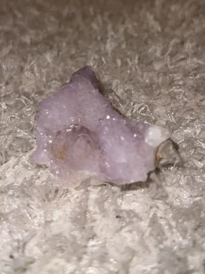 Ljuslila ängelkvarts - Säljer ett ljuslila ängelkvarts med glittrande kristallyta. Stenen har en naturlig, ojämn form och skimrar i olika nyanser av lila och vitt. Perfekt som dekoration eller till kristallsamlingen.