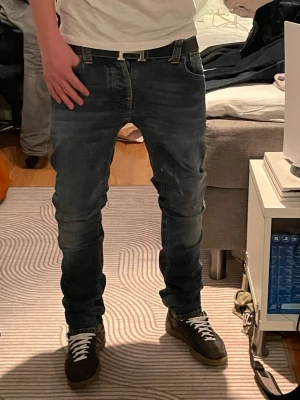 Mörkblå jeans från Nudie Jeans grim Tim - Säljer ett par mörkblå jeans från Nudie Jeans med klassisk femficksmodell och snygga kontrastsömmar på bakfickorna. Jeansen har rak passform och är tillverkade i denim med lätt tvättad look. Perfekta för en avslappnad och stilren outfit.