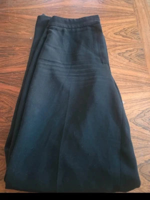 Svarta kostymliknande byxor - Snygga svarta byxor med hög midja och pressveck. Klassisk rak passform och diskreta fickor i sidorna. Perfekta till en stilren look och passar till många olika outfits. Materialet känns mjukt och har en lätt stretch.