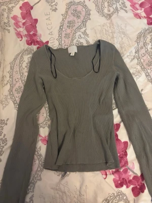 Ribbad grön långärmad topp - Trendig ribbad topp i grönt med långa ärmar och en snygg, djup urringning. Materialet är stretchigt och följsamt, vilket ger en smickrande passform. Perfekt att matcha med jeans eller kjol för en cool vardagslook.