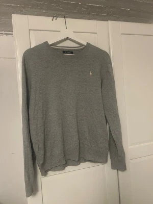 Grå tröja från Polo Ralph Lauren -       ‼️Det står XL men passar som XS/S‼️Klassisk grå tröja från Polo Ralph Lauren med rund halsringning och diskret broderad logga på bröstet. Tröjan har långa ärmar och ribbade muddar vid ärmslut och nederkant. Perfekt för en stilren och avslappnad look. 