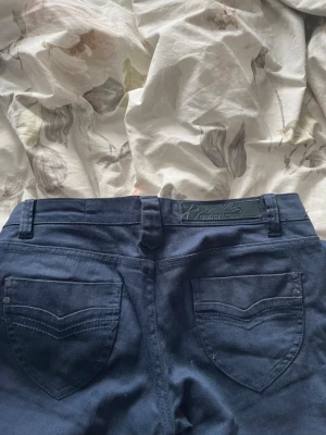 Mörkblå bootcut jeans från Replay - Snygga mörkblå jeans från Replay med bootcut-modell och klassiska bakfickor med dekorativa sömmar. Jeansen har bälteshällor och en läderpatch med Replay-logga bak i midjan. Perfekta för dig som gillar en tidlös och trendig look.