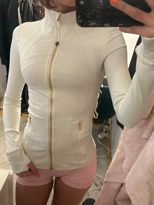 Vit sportjacka med dragkedja - Säljer en vit, figurnära sportjacka med hel dragkedja framtill och två fickor med guldfärgade dragkedjor. Fick den i present men inte kommit till användning så endast testad!