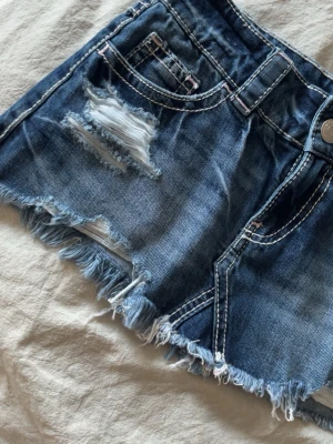 Blå jeanskjol med slitna detaljer - Kort jeanskjol i blå denim med slitna partier och fransig nederkant. Klassiska fickor fram och bak, samt dekorativa sömmar. Perfekt för en avslappnad och trendig look. den är endast testad så den har inge defekter eller så!😊💞 