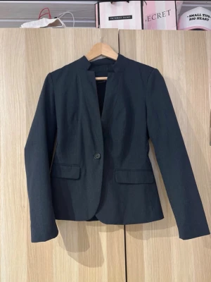 Svart kavaj från Zara Basic - Stilren svart kavaj från Zara Basic Collection med klassisk passform och en knapp framtill. Kavajen har två fickor med lock och är tillverkad i ett slätt material med fodrad insida. Perfekt för att skapa en snygg och modern look.