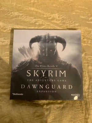 Skyrim Dawnguard Expansion - The Elder Scrolls V: Skyrim The Adventure Game Dawnguard Expansion är ett brädspelstillägg med fantasytema. Boxen är fyrkantig och har en mörk design med motiv av Dovahkiin. Innehåller kort, figurer och spelmaterial i plast och papper. Perfekt för Skyrim-fans som vill utöka sitt äventyr. Ny pris:939kr