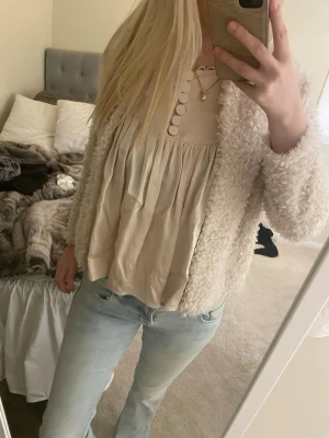 Krämvit fluffig cardiganjacka - Mysig och fluffig cardiganjacka i krämvit färg. Jackan har en kortare, rak passform och är tillverkad i ett mjukt, teddyliknande material. Perfekt för lager på lager och ger en trendig look. (Köp både blusen och koftan och få 10% rabatt!!)