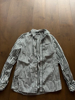 Randig skjorta från J.Lindeberg - Säljer en snygg skjorta från J.Lindeberg med gröna och vita vertikala ränder. Skjortan har klassisk krage, knäppning framtill och lång ärm med manschett. Tillverkad i mjuk bomull som känns skön mot huden. Perfekt för dig som gillar stilrena detaljer.