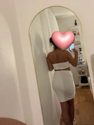 Vitt tvådelat set med kjol och topp - Säljer ett vitt tvådelat set med en tight, midilång kjol och en bandeau topp. Setet har en enkel och stilren design, perfekt för dig som gillar minimalistiskt mode. Materialet är stretchigt och följsamt för en snygg passform.