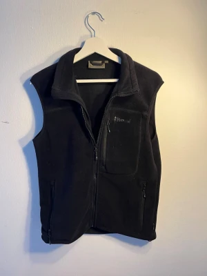 Svart fleeceväst från Pinewood - svart fleeceväst från Pinewood med hög krage och dragkedja framtill. Västen har tre fickor med dragkedja, varav en på bröstet. Perfekt lager för kyliga dagar och enkel att matcha med olika outfits.