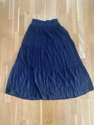 Svart långkjol med resårmidja - Lager 157 kjol för dam i storlek XL. Kjolen är svart och tillverkad i viskos. Modellen är lång med flera sydda partier som ger ett lätt rynkat fall. Resår i midjan för bekväm passform. Passar som vardags- eller sommarkjol. Modell Bella.  Sparsamt använd och i fint begagnat skick   Mått Midjan: ca 36 cm Total längd: ca 97 cm  100% viskos  Kommer från ett djur och rökfritt hem