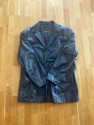 Svart skinnjacka från Rock n Blue - Säljer en svart skinnjacka från Rock n Blue i klassisk modell med krage och knäppning framtill. Jackan har tre fickor på framsidan och en stilren, rak passform. Perfekt för dig som vill ha en tidlös och cool look.