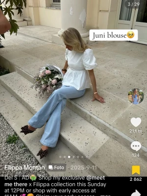 Vit Juni blus med puffärm och rosett - Supersöt vit blus från meet me there x Filippa med puffiga korta ärmar, öppen rygg och stor rosett bak. Blusen har en luftig, utsvängd passform och knytband i nacken. Perfekt för dig som vill ha en trendig och romantisk look.