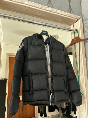 Svart pufferjacka med huva - Säljer nu min D.brand jacka då den har kommit att blivit för liten. Den har lite skavanker men är fullt användbar och varm! 