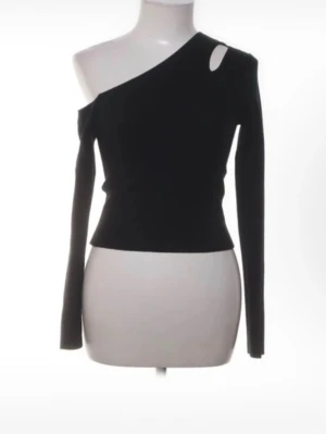 Svart oneshoulder topp med cut-out - Trendig svart oneshoulder topp med lång ärm och en snygg cut-out detalj vid axeln. Toppen har en tight passform och är perfekt för dig som vill sticka ut. Tillverkad i mjukt material som sitter skönt mot kroppen.