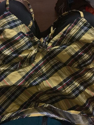 Gul rutig linnetopp med knyt - Trendig gul och svart rutig linnetopp med smala axelband och knyt framtill. Perfekt för dig som gillar färgstarka plagg med coola detaljer. Lätt och luftig känsla, passar till jeans eller kjol.