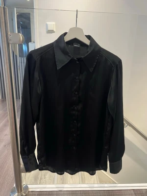 Svart satinskjorta från Gina Tricot, XS - Säljer en svart långärmad skjorta från Ginatricot i glansigt satinmaterial. Använt den 1-2 gånger💖