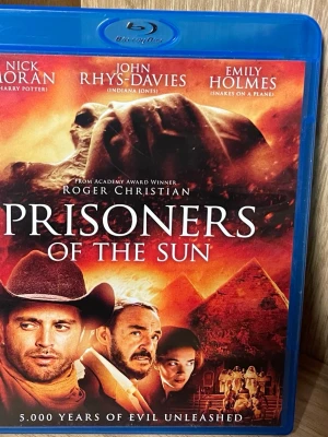 Prisoners of the Sun Blu-ray - Blu-ray-film med titeln 'Prisoners of the Sun'. Omslaget har motiv av egyptiska pyramider, en sfinx och äventyrstema. Filmen har skådespelare som Nick Moran, John Rhys-Davies och Emily Holmes. Text på svenska och engelska på baksidan.