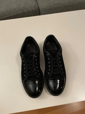Svarta sneakers med lackad tå - Snygga helsvarta sneakers med cool lackad tå och klassisk snörning. Ovandelen är i mockaliknande material och sulan är svart. Perfekta för dig som gillar stilrena och moderna skor med en twist.