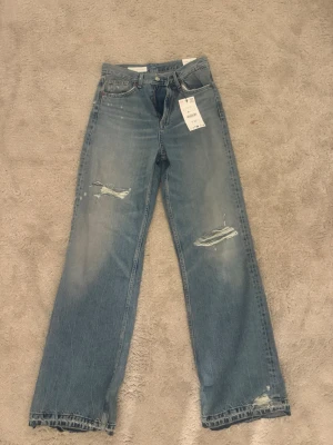 Zara blå raka jeans med slitningar - Säljer ett par blå raka jeans från zara med coola slitningar på benen och bakfickan.