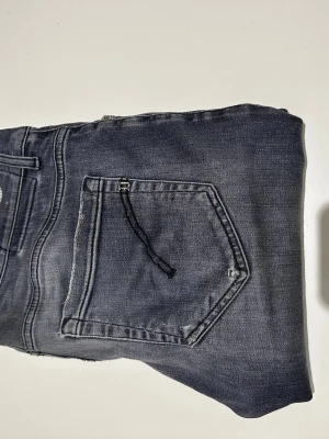 Dondup George  - Snygga mörkgrå skinny fit jeans från Dondup med klassisk femficksdesign och dragkedja. Jeansen har en tvättad look och är tillverkade i stretchigt denimtyg för extra komfort. Perfekta för dig som gillar en smal siluett och modern stil. Defekt vid låret därav lägre pris men det har fixats hos en skräddare. Modellen är 187 och väger 70kg. Vid frågor är det bara att skriva!