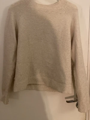 Beige stickad tröja med rund hals - Mysig beige stickad tröja med rund halsringning och långa ärmar. Tröjan har ribbade muddar vid ärmslut och nederkant, samt en något lös passform. Perfekt för kalla dagar och enkel att matcha med olika outfits.
