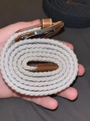 Beige flätat bälte med skinn-detaljer - Snyggt beige flätat bälte med bruna skinn-detaljer och silvrigt spänne. Perfekt accessoar för att lyfta din outfit med en stilren touch. Bältet har en klassisk design och passar till många olika looks.