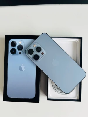 iPhone 13 Pro Sierra Blue 128GB - Snygg iPhone 13 Pro i färgen Sierra Blue med stilren design och platt baksida i glas. Telefonen har tre kameror, rostfria kanter och levereras i originalkartong med laddningskabel. Perfekt för dig som vill ha en kraftfull och modern smartphone. batteri 78%