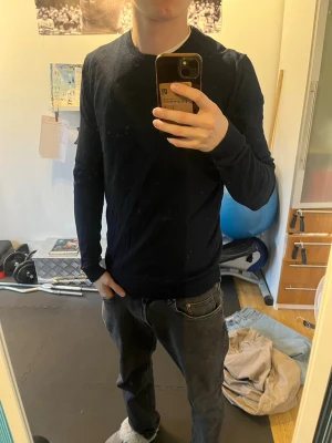 Mörkblå långärmad tröja - En enkel och stilren mörkblå långärmad tröja med rund hals. Tröjan har en smal passform och är tillverkad i ett mjukt, tunt material som passar perfekt till vardagslooken. Inga synliga loggor eller detaljer.