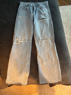 Ljusblå slitna raka jeans - Säljer ett par ljusblå jeans från Zara med raka ben och flera slitningar och hål framtill. Jeansen har råa, fransiga benslut och klassisk femficksmodell. Perfekta för en avslappnad och trendig look. Bara testade men ingen prislapp kvar 