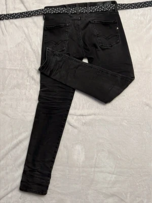 Svarta skinny jeans från Replay - Säljer ett par svarta skinny jeans från Replay med klassisk femficksmodell och diskreta sömmar. Jeansen har en smal passform och är tillverkade i stretchigt material för extra komfort. Perfekta för en trendig och avslappnad look.
