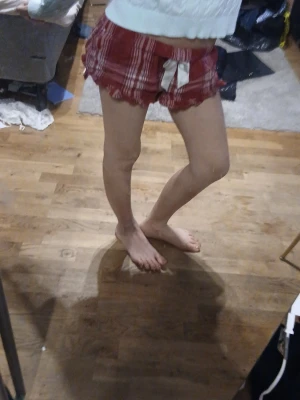 Lowwaist pyjamas shorts stl xs 158/164 - Säljer ett par rödrutiga pyjamasshorts med vit rosett framtill och volangkant. Shortsen har en avslappnad passform och elastisk midja för extra komfort. Perfekta för mysiga hemmakvällar eller lata morgnar. 