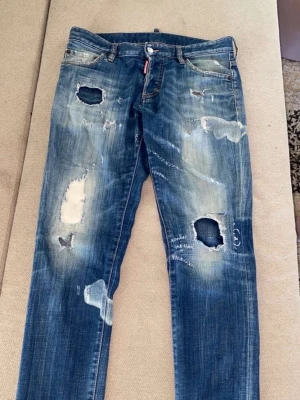 Blå  jeans från Dsquared2 - Säljer ett par blå slim fit jeans från Dsquared2 med kraftiga slitningar, hål och blekta detaljer. Jeansen har en modern, trendig look med flera trasiga partier och är tillverkade i denim. Perfekta för dig som gillar streetwear och edgy stil.