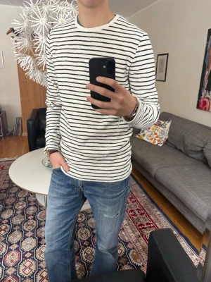 Randig långärmad tröja  - Vit långärmad tröja med blåa horisontella ränder. Tröjan har en klassisk rund halsringning och är gjord i mjuk bomull. 